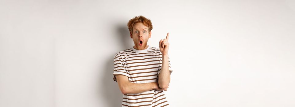 Excited redhead man having revalation, raising finger in eureka sign and saying idea, standing over white background.