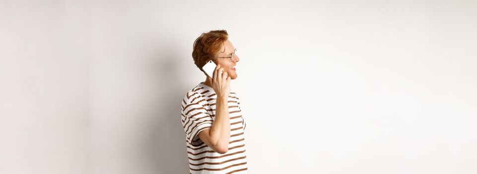 Profile of happy young handsome man talking on mobile phone, looking left and smiling, standing over white background.