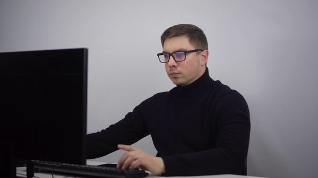 Young IT specialist works at the computer typing on the keyboard. A man with glasses sits in the office at the workplace. 4k