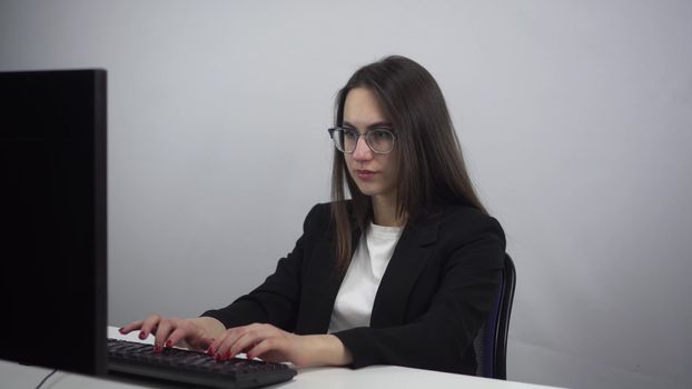 Businesswoman works on a computer in the office. A young woman in a suit and glasses carefully types on the keyboard. 4k