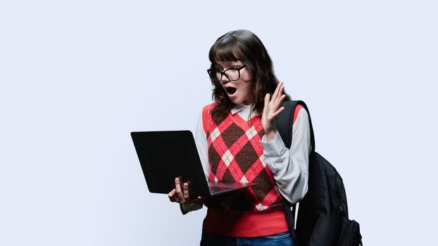 Surprised female student 18, 19 years old looking in laptop on white studio background. Indignant anxious girl in glasses using internet for study, e-learning, online lessons, college university courses