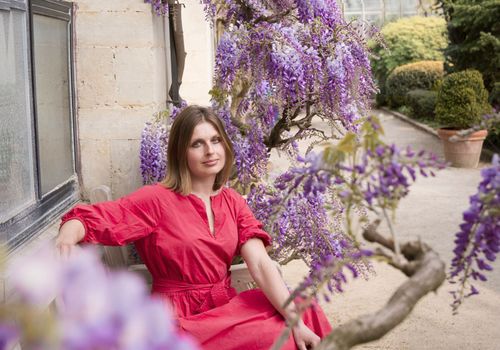 beautiful young woman in red dress sits on a bench in the thickets of blooming wisteria. High quality photo