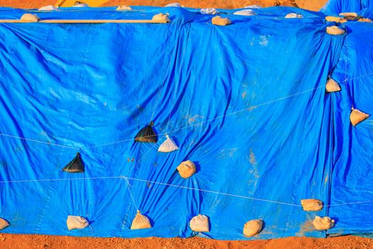 Large blue tarp held down by sandbags covers materials outdoors. High quality photo