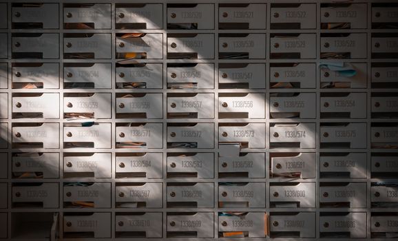 Bangkok, Thailand - 28 Jan, 2023 - Beautiful sunlight shine on rows of white wooden mailboxes with keyholes for resident in condominium or apartment. Postbox in condo, Light and shadow, Selective focus.