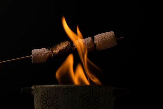 skewer of sweet marshmallows warming in the fire on a black background