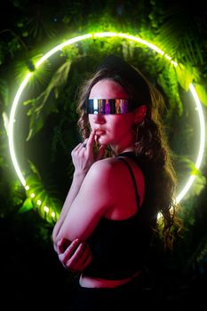 Caucasian woman in panoramic sunglasses against the background of an annular neon lamp in plants