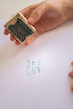 woman's hands placing a sustainable packaging stamp on a blank sheet of paper