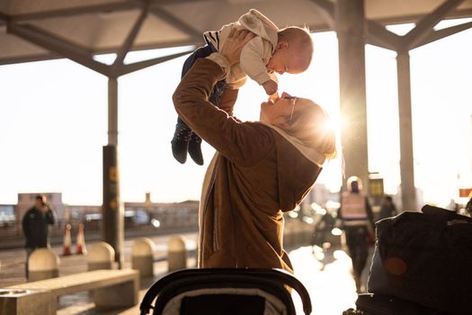 Motherat happily holding and lifting his infant baby boy child in the air after being rejunited in front of airport terminal station. Baby travel concept