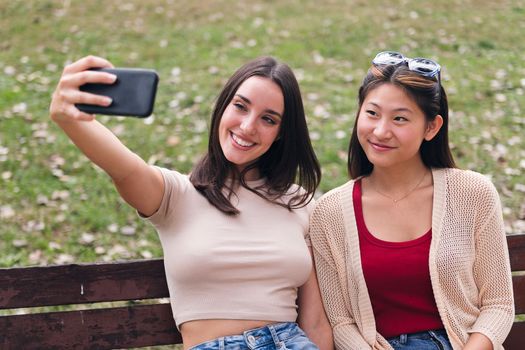 two young women smiling happily while taking a selfie photo with the mobile phone, concept of fun and technology
