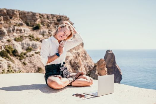 Happy girl doing yoga with laptop working at the beach. beautiful and calm business woman sitting with a laptop in a summer cafe in the lotus position meditating and relaxing. freelance girl remote work beach paradise
