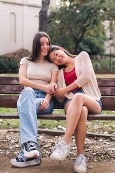 happy young female couple sitting on a park bench during their romantic date, concept of friendship and love between people of the same sex