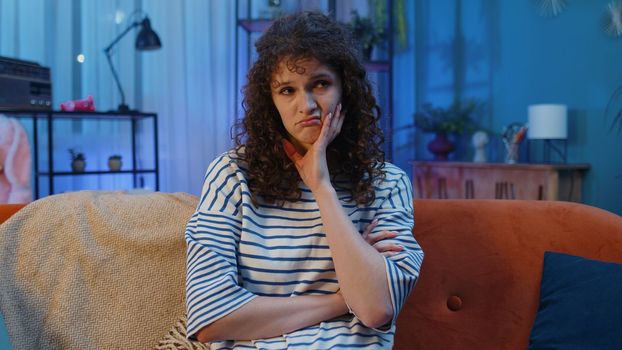 Sad lonely woman sitting at home looks pensive thinks over life concerns or unrequited love suffers from unfair situation. Unhappy sick girl problem, break up, depressed feeling bad annoyed burnout