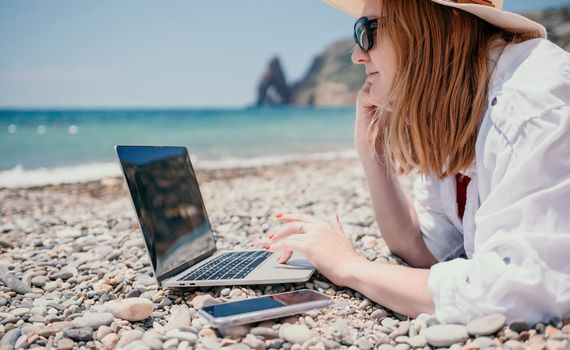 Woman sea laptop. Business woman in yellow hat working on laptop by sea. Close up on hands of pretty lady typing on computer outdoors summer day. Freelance, digital nomad, travel and holidays concept