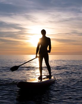 a sporty guy swims with a paddle on a sapboard in the sea under the beautiful sunset sun