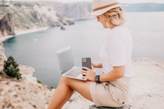 Digital nomad, Business woman working on laptop by the sea. Pretty lady typing on computer by the sea at sunset, makes a business transaction online from a distance. Freelance remote work on vacation