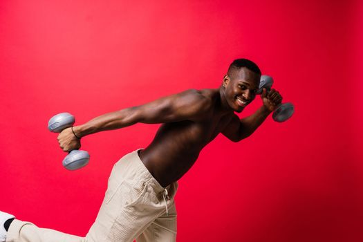 Portrait of happy african man with dumbbells over red background