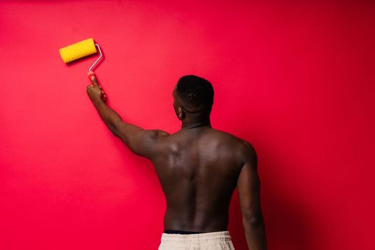 African painter focused on work holding professional roller to paint interior wall, studio.