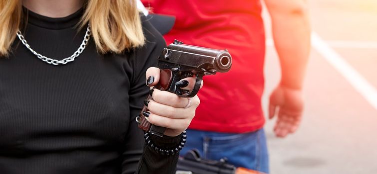 A young girl with a gun in her hands. Makarov pistol in young hands with black manicure.