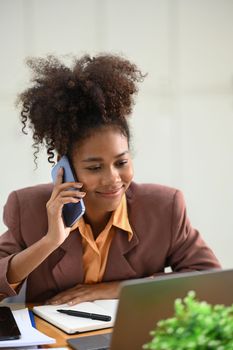 Smiling African American businesswoman in stylish suit having pleasant conversation while sitting at workstation.