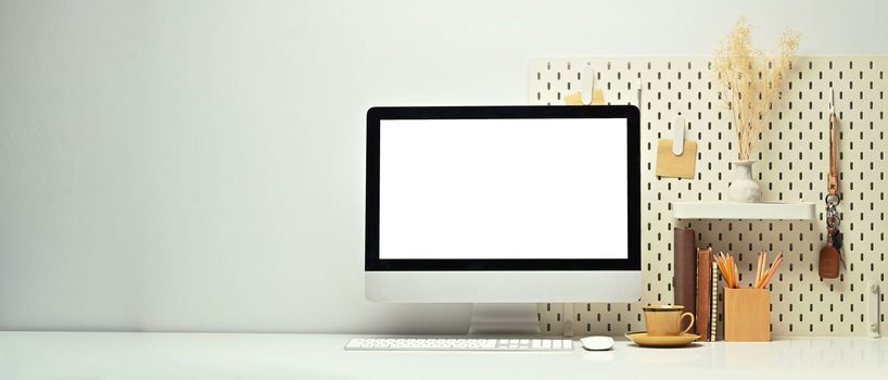 Home office with blank computer monitor, books, coffee cup and pencil holder white table. Copy space for your advertise design.