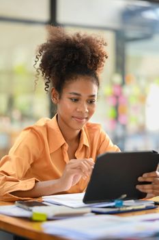Attractive female employee looking at tablet, checking online information at her office desk.
