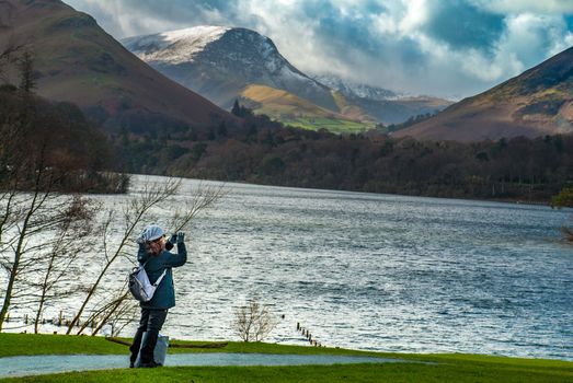 Lake District, UK - apr 15, 2019 : A woman who is taking pictures of the scenery of the lake and the mountains in the Lake District area.