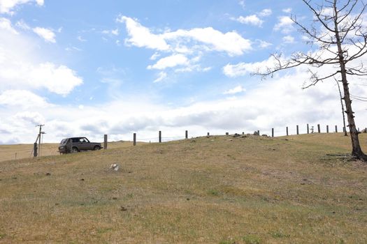 A car drives uphill on Olkhon Island along an old fence