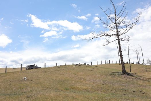 An off-road vehicle drives uphill along a Baikal road along a fence on Olkhon Island
