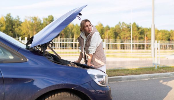 mature woman at the open hood of a broken car.