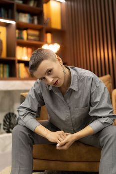 Caucasian style a woman with a short haircut sits in an easy chair on the background of the library.