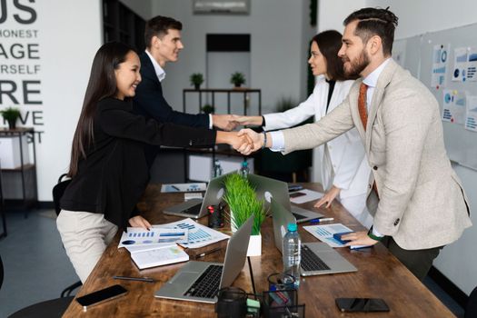 competitors company employees shake hands at a large table after successful negotiations.