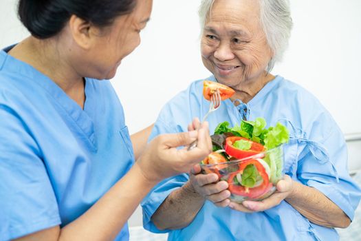 Asian senior or elderly old lady woman patient eating breakfast vegetable healthy food with hope and happy while sitting and hungry on bed in hospital.