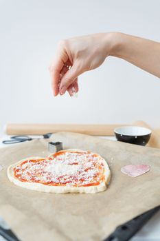 Pizza dough in the shape of a heart, the chef sprinkles the pizza with parmesan cheese. The concept of a surprise for St. Valentine's Day