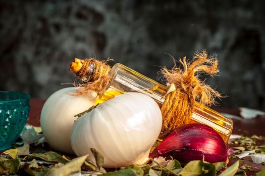 Close up of oil of onion or Allium cepa L oil on a wooden surface with raw onions in dark Gothic colors.This oil Cures Fever,Nourishes The Skin,Heals Wounds,Helps In Breathing and Cold Healer etc.