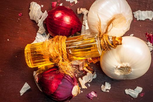 Close-up of oil of onion or Allium cepa L oil on a wooden surface with raw onions in dark Gothic colors. This oil Cures Fever, Nourishes The Skin, Heals Wounds, Helps In Breathing and Cold healers, etc.