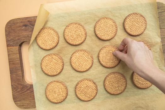 Woman hand taking freshly baked normal grain healthy cookie top view, on wooden plate