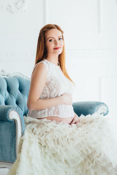 red-haired pregnant young girl in a blue armchair of a bright room