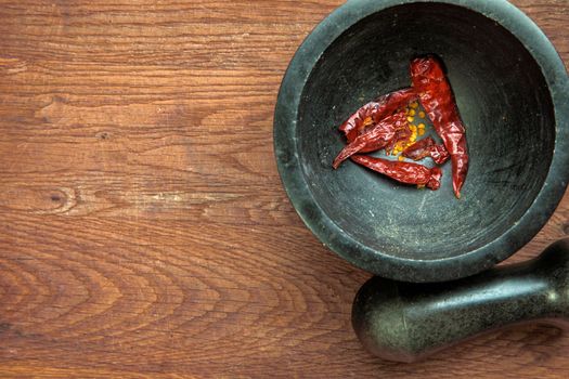 Red hot pepper in a stone granite mortar, dried chillies crunched top view on wooden background copy space healthy food