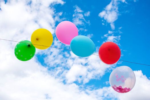 Colorful party balloons in front of a blue cloudy sky.