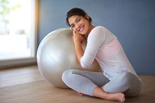 Make it a lifestyle, not a duty. Full length shot of a sporty young woman leaning on a pilates ball against a grey background