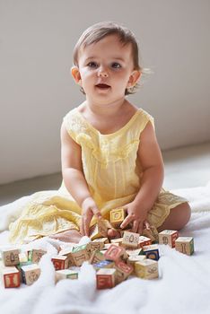 Shes so curious. a cute baby girl sitting on the floor playing with toy blocks