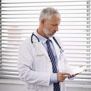 Technology is vital for advancing healthcare. a mature male doctor using a digital tablet