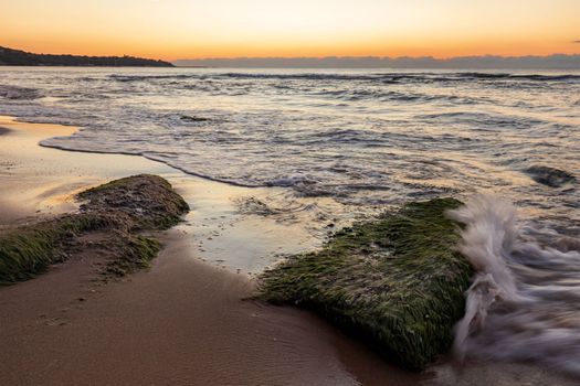 Seascape view with rocks with moss and small wave splash.