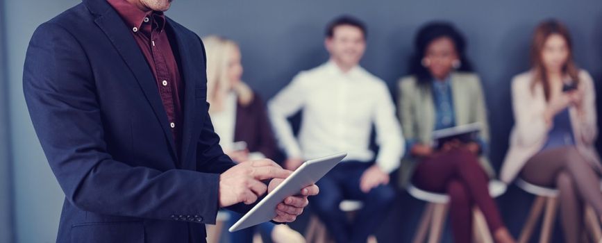 Technology is at the forefront of most success. an unrecognizable businessman using a tablet with his colleagues in the background