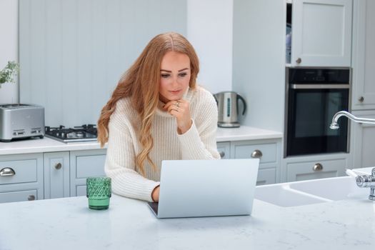 Remote Work. Beautiful middle age Freelancer Lady Working With Laptop In Kitchen, Happy Woman Using Computer At Home, Sitting At Table In Cozy Interior, Enjoying Online Job, Free Space