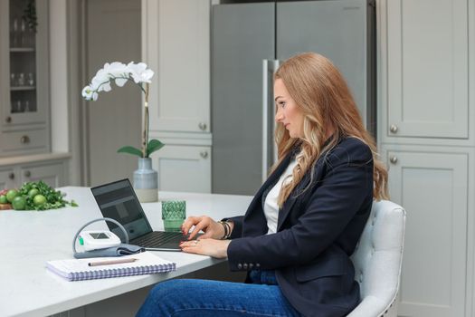 Remote Work. Beautiful middle age Freelancer Lady Working With Laptop In Kitchen, Happy Woman Using Computer At Home, Sitting At Table In Cozy Interior, Enjoying Online Job, Free Space