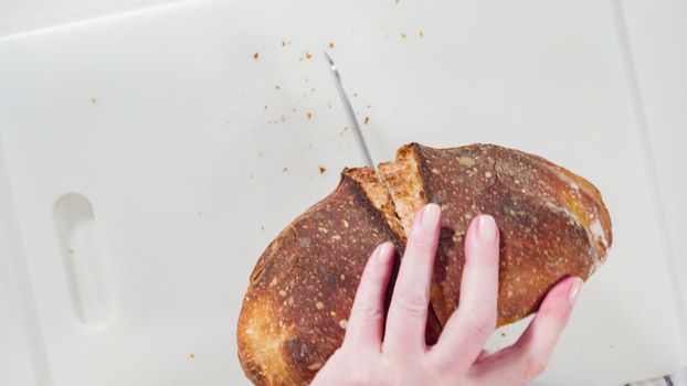 Flat lay. Slicing freshly baked sourdough wheat bread on a white cutting board.