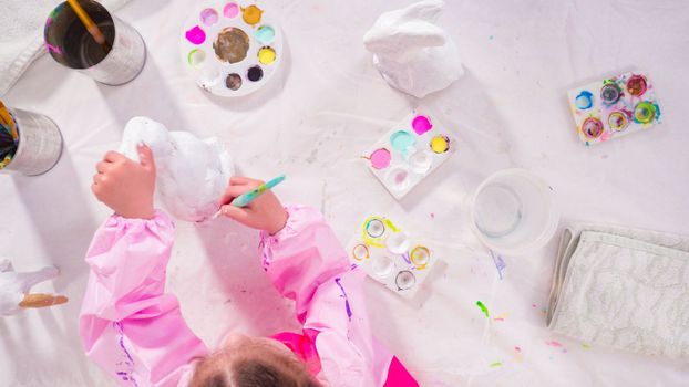 Flat lay. Little girl painting paper mache figurine at homeschooling art class.