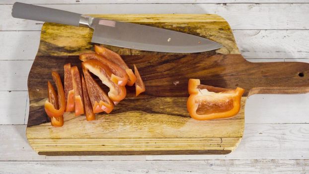 Mincing organic red bell peppers on a wood cutting board.