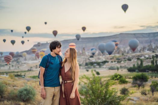 Tourists couple man and woman looking at hot air balloons in Cappadocia, Turkey. Happy Travel in Turkey concept. Couple man and woman on a mountain top enjoying wonderful view.